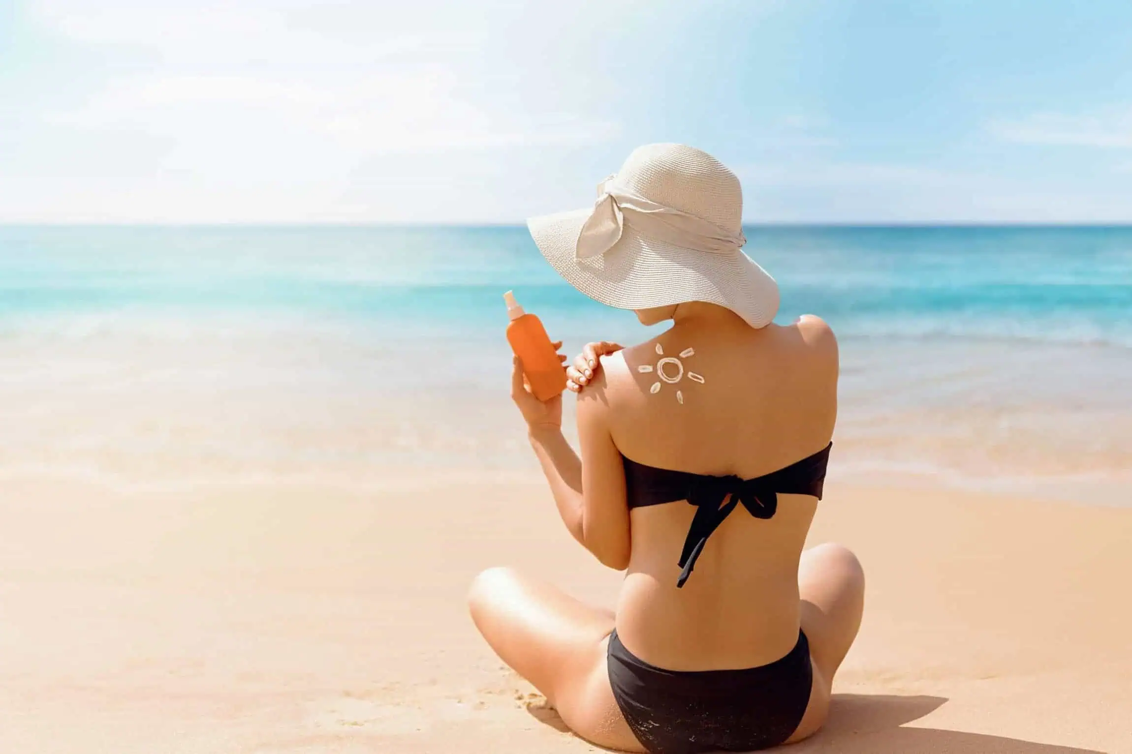 a woman in a garment and hat applying sunscreen on her shoulder | Reclaim Med Spa and Wellness | St Louis, MO